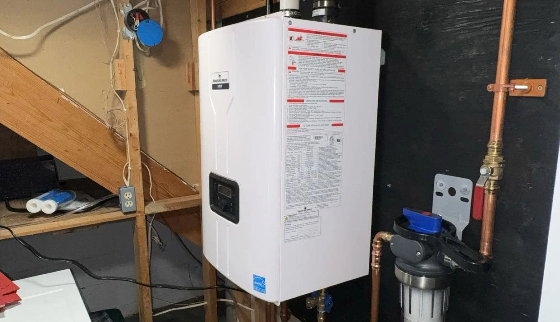 A white tankless water heater and water filtration system mounted on a black wall in a utility room.
